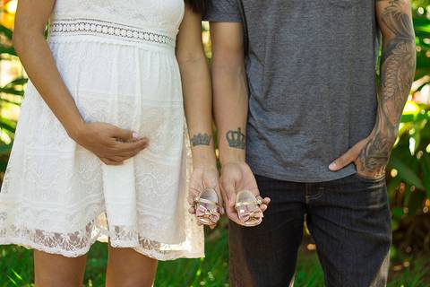 Pais posam mostrando tatuagens iguais, em homenagem a bebê. Mostram os sapatinhos'