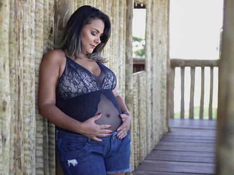 Gestante na casinha do parque das barrigudas, de short e body, acaricia e olha para barriga'