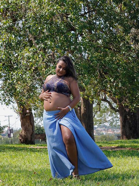 Gestante posa no parque, sob o sol. olha e acaricia a barriga'