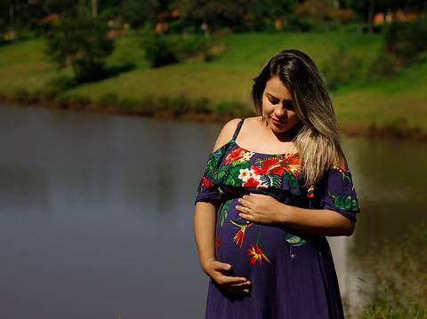 Gestante pose com vestido azul estampado, marcando a barriga. Ao fundo lago do parque'