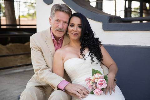 Noivos, sentados no banco se abraçam e sorriem para camera'