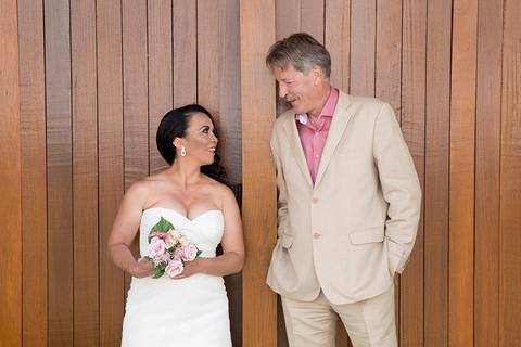 Noivos, posicionados na parede de madeira, lada a lado se olham nos olhos'