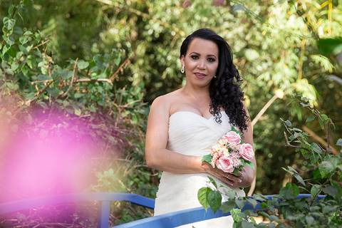 Noiva posa olhando para câmera com seu buquê na ponte. Retrato meio corpo com flor em desfoque no primeiro plano'