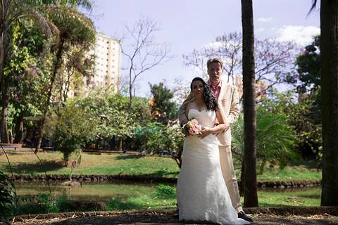 Noivos posam abraçados, plano aberto mostra toda vegetação e lago ao fundo'