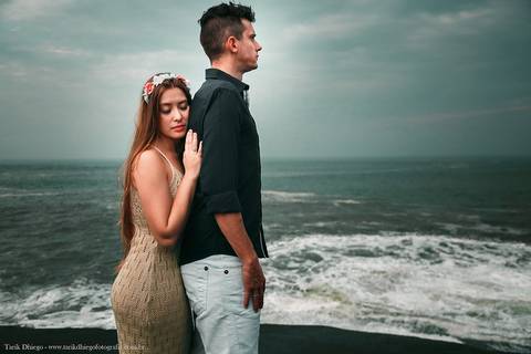 Noivos nas pedras e céu na praia no ensaio pré-wedding na praia casal riviera de são lourenço bertioga são paulo noiva deitada nas costas do noivo'