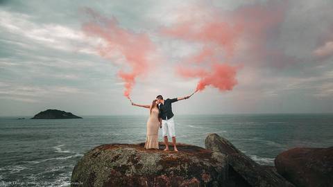 Noivos nas pedras com bastão de fumaça rosa durante o ensaio pré-wedding na praia de Riviera de São Lourenço - são paulo'