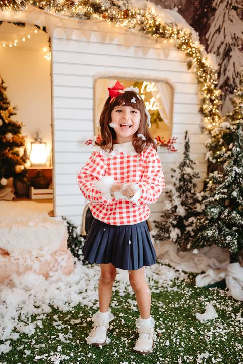 menina segurando floco de neve em cenário natalino com trailer ao fundo. arvores de natal no canto'