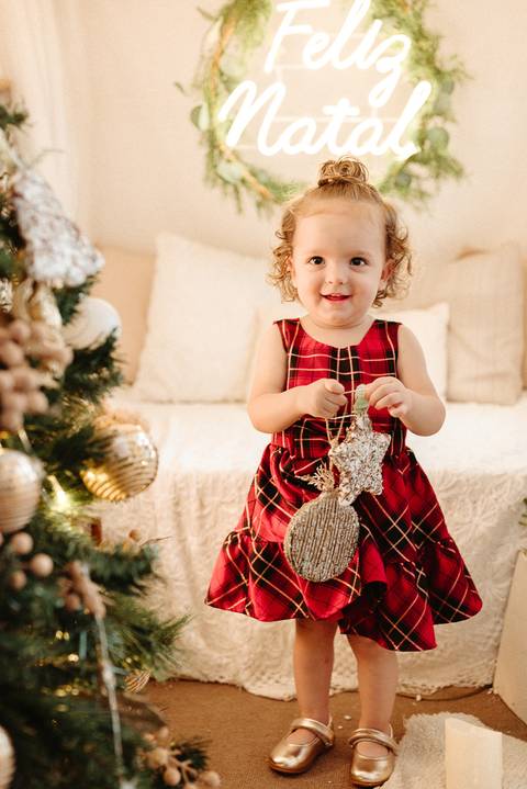 menina loira segurando uma estrela e bola de natal efeito rústica. ela tem cabelos curtos enrolados e esta sorrindo'