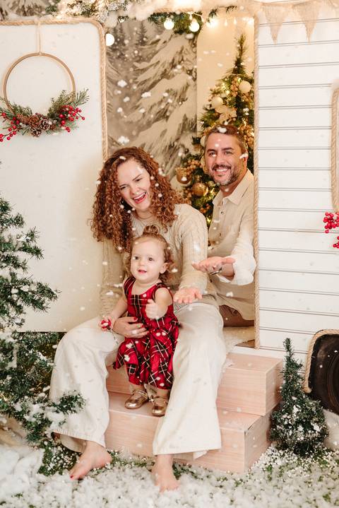 família sentada em frente a um trailer natalino com neve realista caindo. '