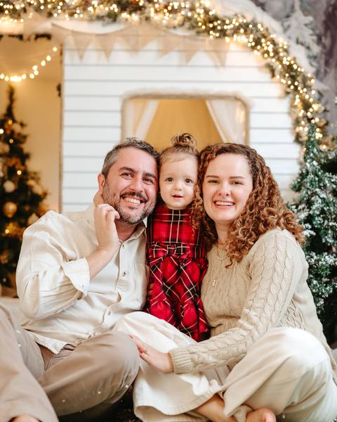 pai, mãe e filha olhando para a câmera com rostos juntos. ao fundo cenário de natal trailer natalino'