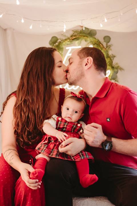 pai e mãe dando um beijo e filha olhando para a câmera'