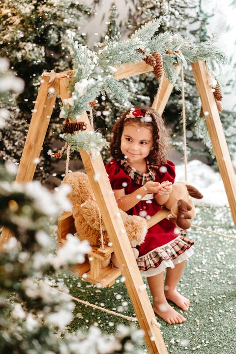 menina de cabelos enrolados, segurando pelúcias e sentada em um balanço infantil.'