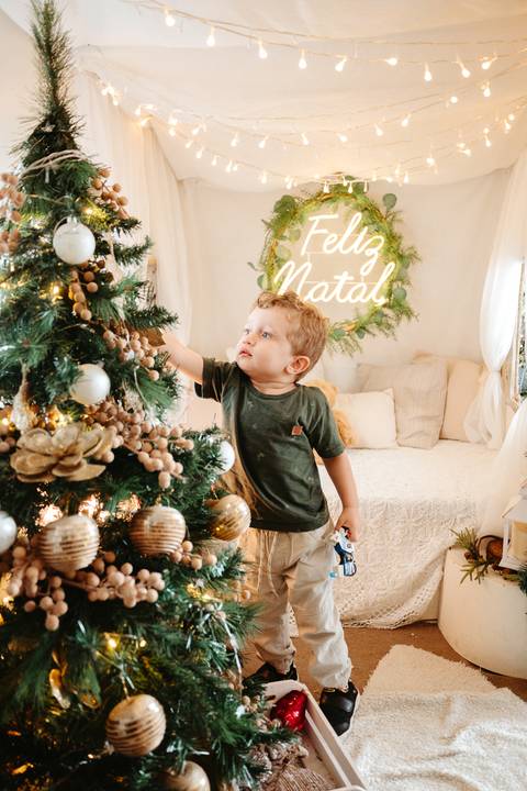 menino de aproximadamente 1 ano e meio enfeitando uma Arbore de natal com tema natalino'