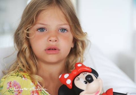 Menina loira, olhos claros, vestido amarelo floral.'