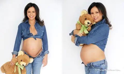 Gestante usando calça e camisa jeans, segurando um urso de pelúcia. '