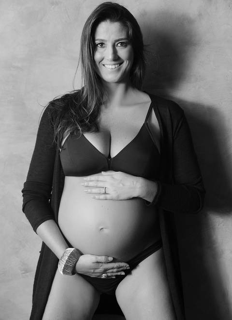 Gestante, imagem frontal, com as mãos sobrepostas sobre a barriga, fotografia p&b.'