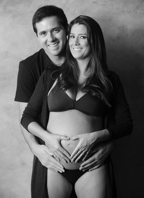 Casal abraçado, imagem fontal, ambos sorrindo, mulher grávida, fotografia p&b.'