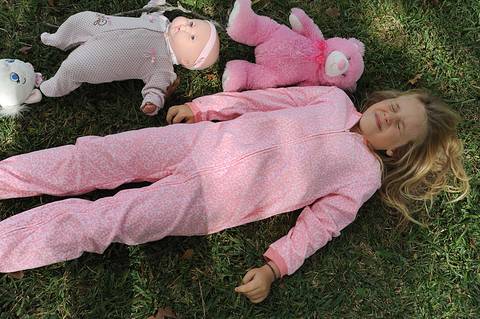Menina loira usando pijama rosa, posa com seus brinquedos em ensaio fotográfico .'