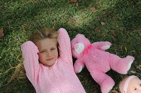 Menina loira, olhos claros, com pijama cor de rosa e brinquedos.'