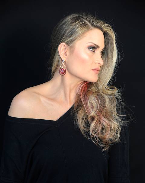 Mulher loira de perfil com mechas cor de rosa e blusa preta.'