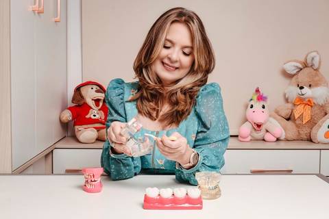 retrato corporativo com consultoria de imagem Niterói foto da dentista mostrando prótese. Ela está em sala de atendimento com ursos de pelúcia.'