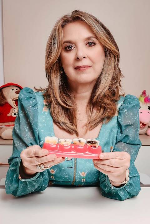 fotógrafo para branding pessoal Niterói foto da dentista mostrando prótese. Ela está em sala de atendimento e olha para a camera transmitindo seriedade.'