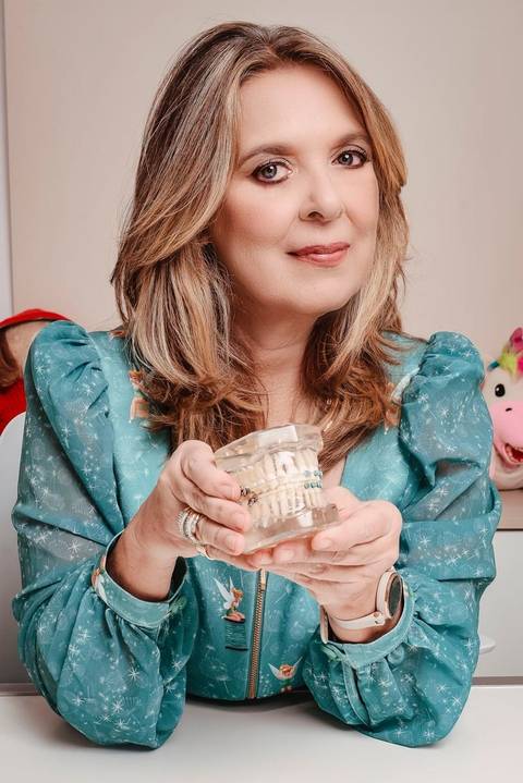 fotógrafo para branding pessoal Niterói em consultório médico de dentista em Icaraí ela mostra uma prótese dentária e olha para a camera transmitindo autoridade e leveza.'