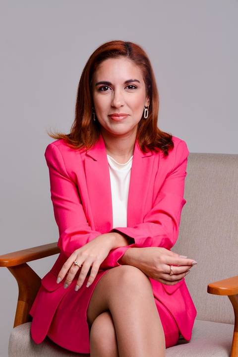 fotografia de retrato em Niterói de empreendora sentada em cadeira moderna com braços de madeira. A empreendedora está com seus braços sobre o colo e sorri levemete para a camera transmitindo muita segurança, autenticidade e poder.'