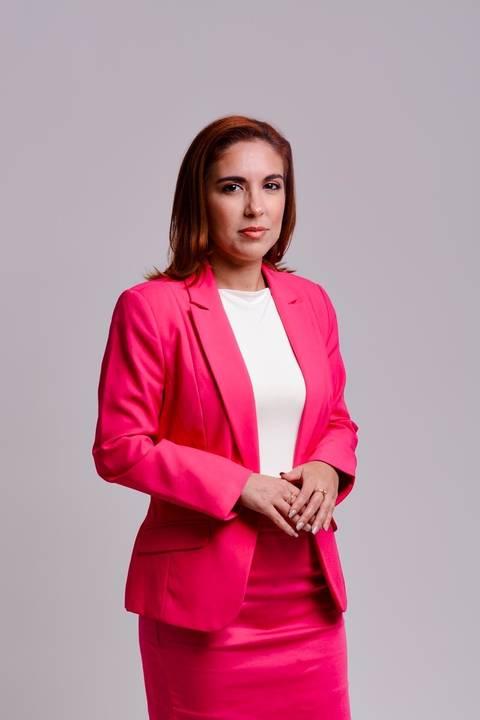 ensaio de marca pessoal em Niterói para empreededora do ramo de beleza. Ela está em pé olhando para camera com olhar sereno e leve sorriso transmitindo segurança e poder. Ela veste blazer rosa, saia rosa e blusa branca.'
