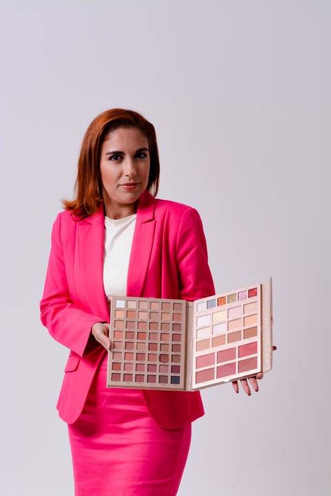 retrato corporativo de empresária em estúdio no centro de Niterói. Ela veste blazer rosa e saia rosa que transmite muita segurança ao segurar um estojo com amostras sombras. Ela olha para a camera com leve sorriso que transmite segurança, confiança.'