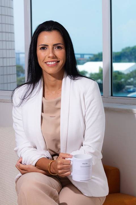 fotografia de marca pessoal de advogada feito em estúdio no centro de Niterói. A advogada está sentada em um sofá e ao fundo uma vista do alto do prédio para o centro de Niterói.'