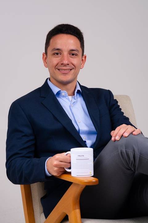 ensaio em estúdio de advogado em estúdio no centro de Niterói. O advogado está centado em cadeira moderna segurando uma caneca e olhando diretamente para a camera.'