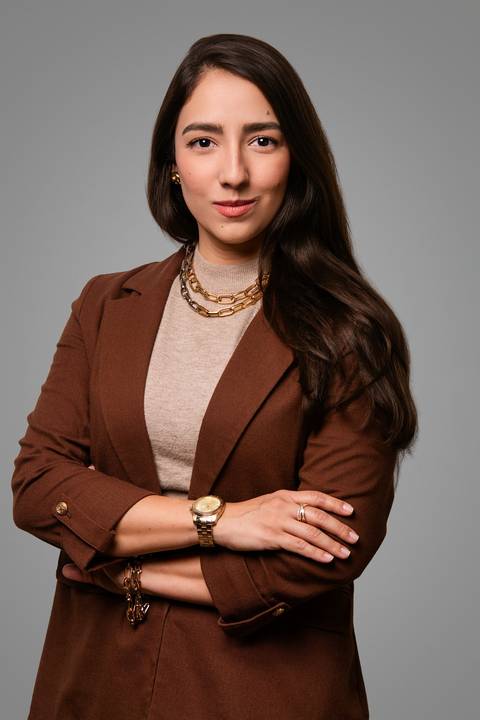 advogada de braços cruzados olhando direto para a camera fundo cinza'