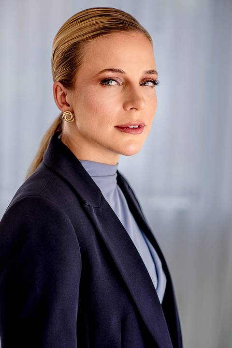 Retrato de perfil da Dra. Lara Poltronieri, com blazer azul-marinho e expressão serena, traduzindo elegância e autoridade médica.'