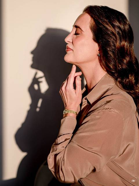 Retrato artístico da Dra. Kátia Blume em perfil lateral, com iluminação direcionada e sombra projetada na parede, explorando a fotografia de posicionamento autoral.'