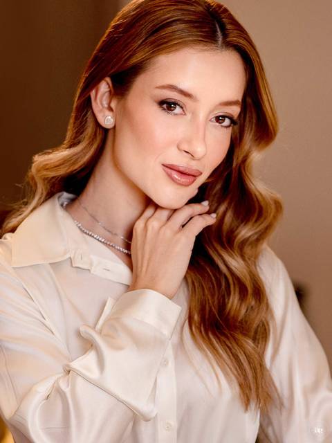 Retrato profissional da biomédica estética Katiane Soares em camisa clara, com mão delicadamente apoiada no rosto e iluminação suave, valorizando sua naturalidade e elegância.'