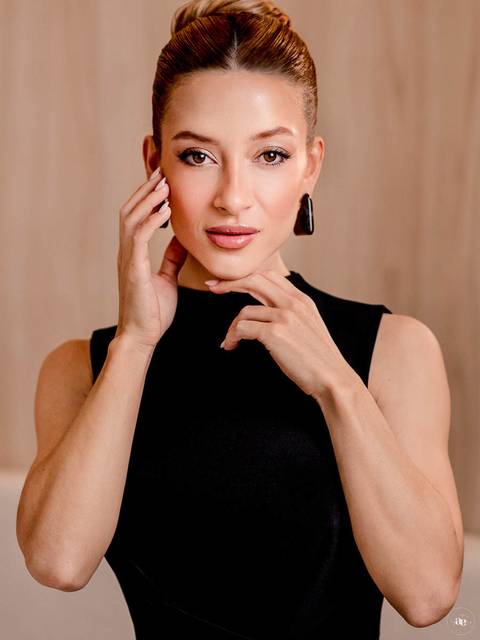 Fotografia profissional da biomédica estética Katiane Soares em traje preto, com mãos delicadamente próximas ao rosto, olhar direcionado à câmera e composição que valoriza sua beleza natural.'