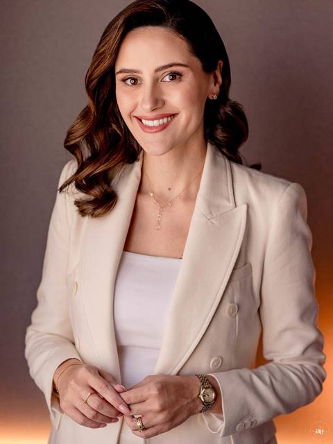 Retrato profissional da dentista Fernanda Wisniewski com sorriso natural, cabelos ondulados e blazer claro, revelando elegância e proximidade na fotografia de posicionamento.'