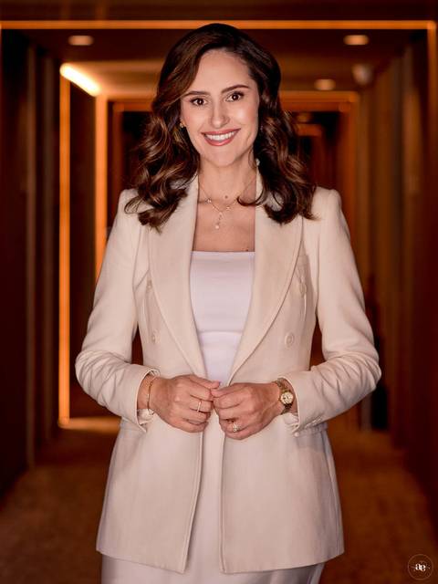 Retrato de autoridade da Dra. Fernanda Wisniewski em blazer claro, com postura frontal e mãos próximas à cintura, em uma composição que valoriza sua imagem como dentista.'
