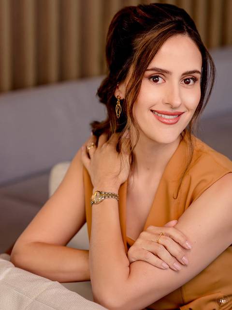 Retrato profissional da Dra. Fernanda Wisniewski em traje caramelo, com sorriso espontâneo e mão próxima ao cabelo, transmitindo naturalidade e proximidade.'