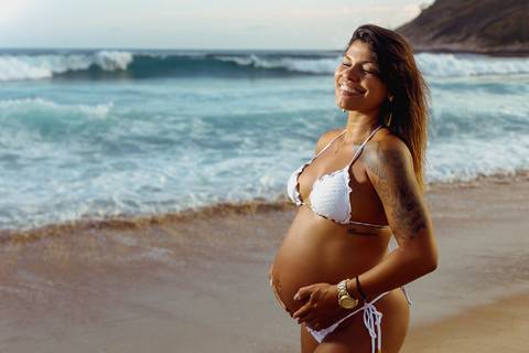 Grávida faz pose de com a mão na barriga e com os olhos fechados em seu ensaio fotográfico/RJ'