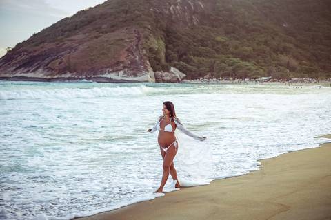 gestante caminhando na praia com os  braços zul'