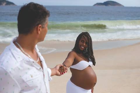 Ensaio gestante externo esposo segura sua mão e ao fundo praia de Camboinhas/RJ'