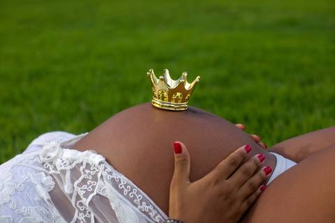 Ensaio externo de gestante ele deitada na grama com coroa na barriga.. em Orla de Camboinhas-Niterói'