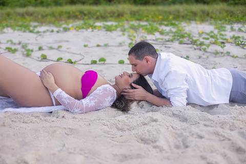 gestante deitada na areia e seu espoa beijando sua testa em ensaio romântico na praia-prainha-RJ'