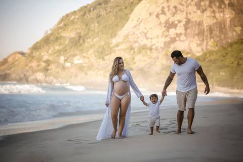 gestante caminhando de mães dadas com filho e marido na prainha em ensaio fotográfico-RJ '
