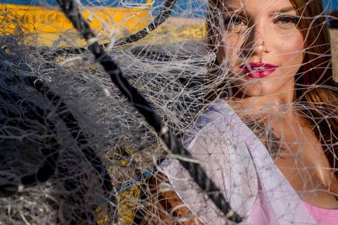 Retrato fotográfico de mulher sentada na areia segurando rede de pesca na praia de Itapuã, Vila Velha - ES'