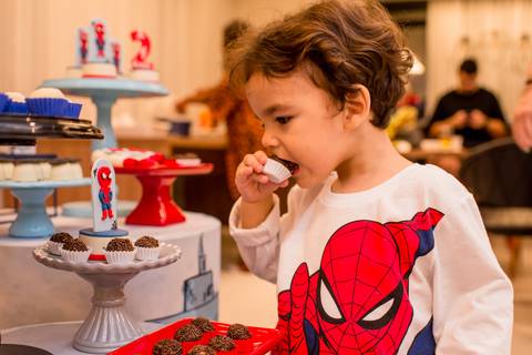fotografia de aniversariante comendo docinho de sua própria festa infantil com tema homem-aranha, realizada em vitória - es'