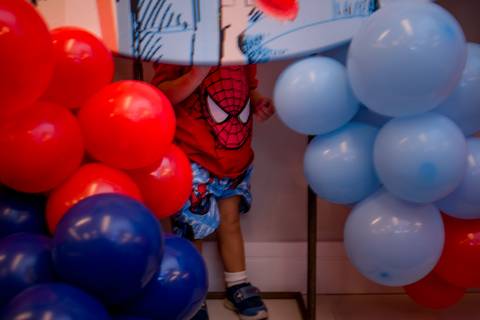 fotografia de aniversariante se escondendo atrás da decoração da sua festa de aniversário de 2 anos. tema: homem-aranha. realizada em vitória - es'