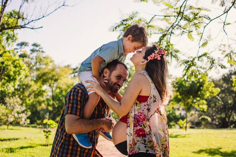 Fotografia ensaio de gestante, Ilha do Frade, Vitória, ES. Fotografia de família. Pai segurando o filho nas costas. Mãe, gestante beijando a testa do filho.'
